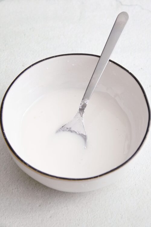 Cream mixture in a white bowl with a metal spoon, used for baking recipes.