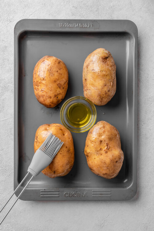Golden baked potatoes on a baking sheet with olive oil and a basting brush.