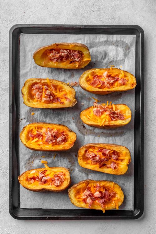 Baked potatoes stuffed with cheese and bacon on a baking sheet.