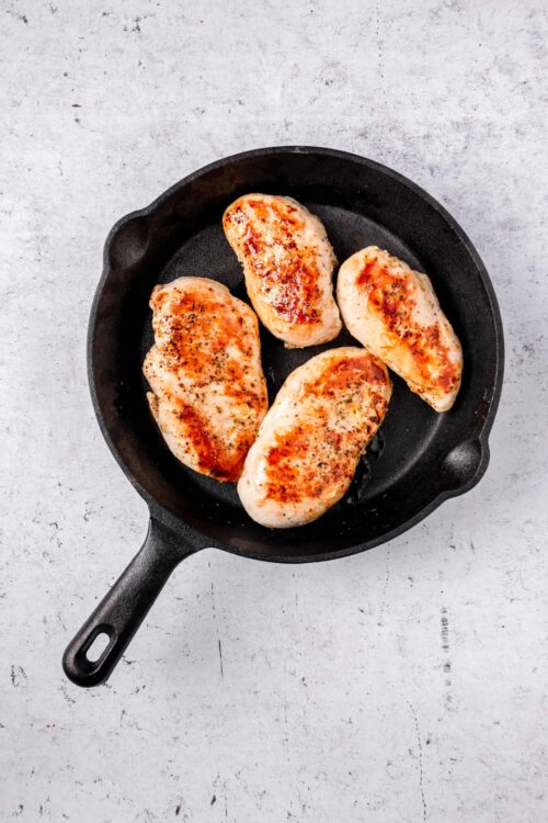 Juicy baked chicken breasts in a black skillet on a light textured surface.