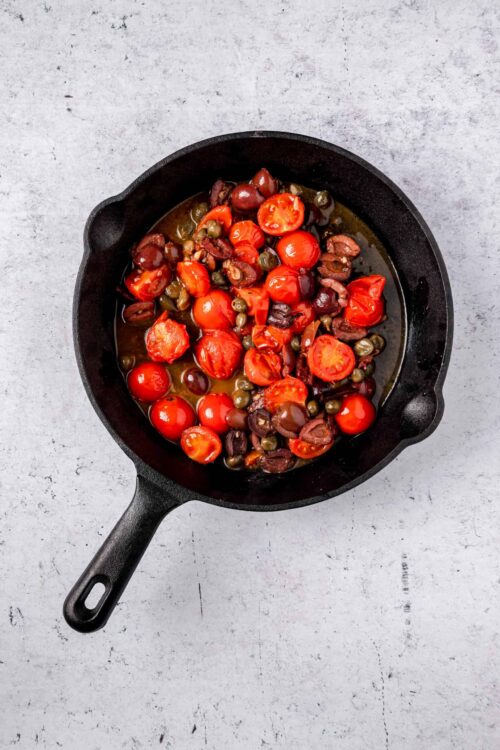 Roasted cherry tomatoes, olives, and herbs in a black skillet.