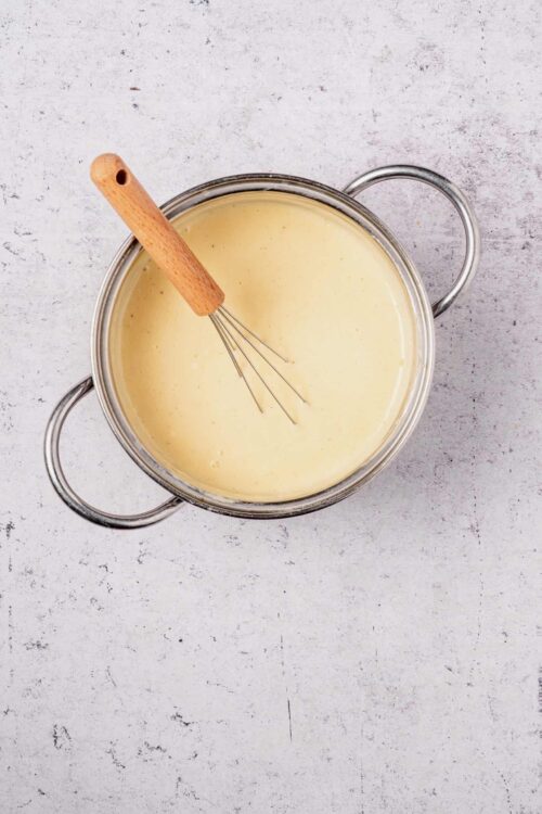 Creamy custard mixture in a stainless steel bowl with a whisk and wooden handle for baking or dessert recipes.