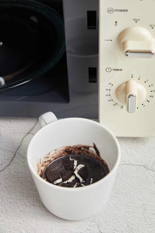 Faded black coffee mug with Oreo cookies remnants on a white textured surface.
