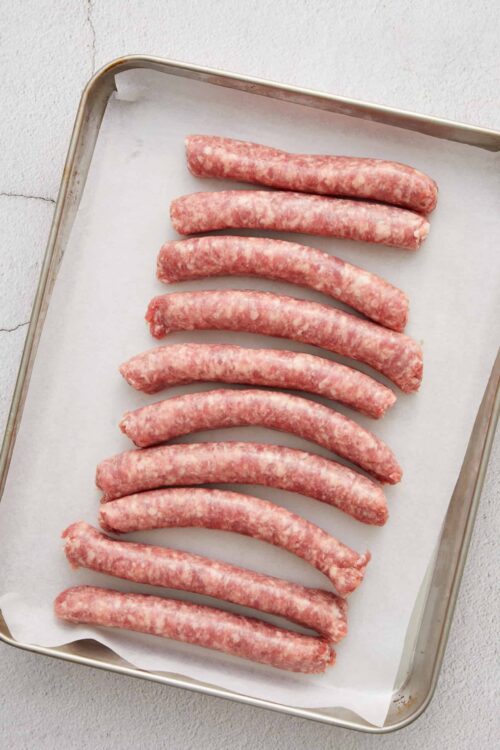 Raw sausage links on a baking sheet for cooking or baking.