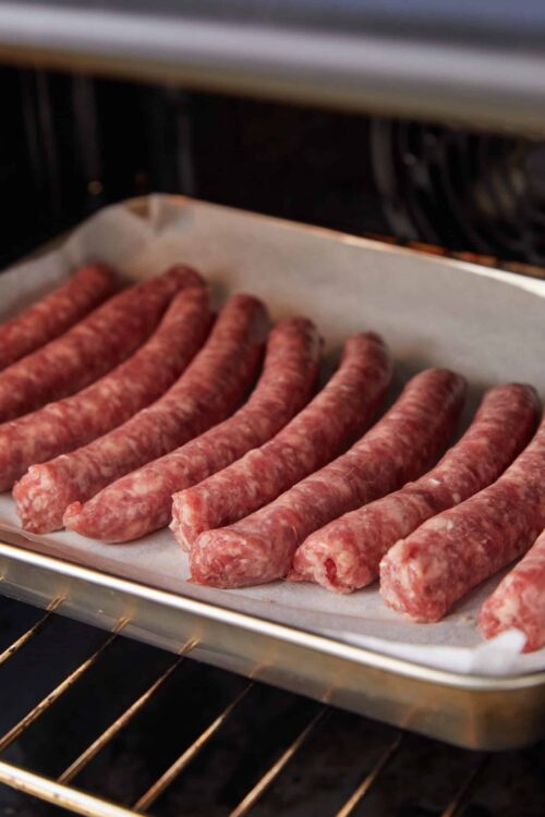 Coiled raw sausages baking in oven on parchment paper.