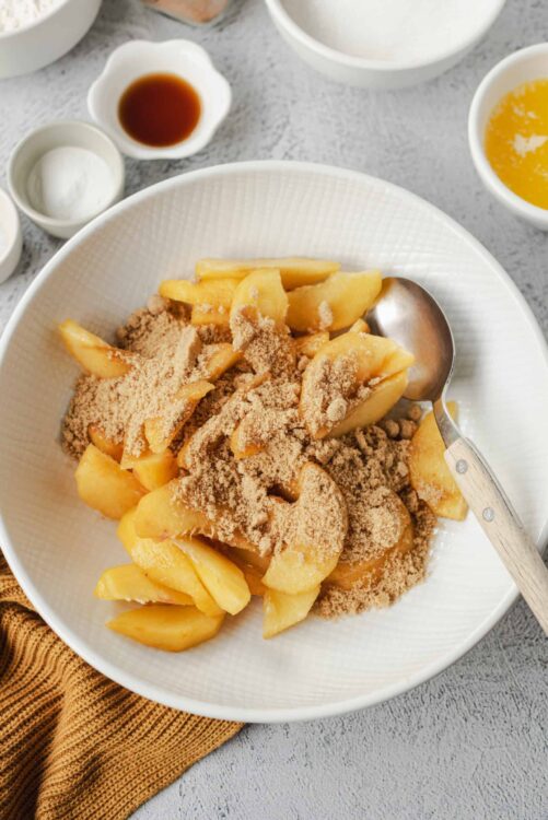 Baked peaches with cinnamon and sugar on a white plate.