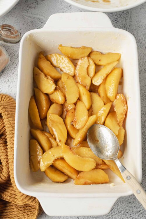 Golden caramelized peach slices in a baking dish preparing for dessert.