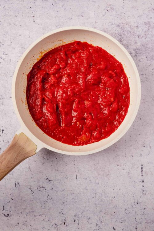 Tomato sauce in a white skillet on a textured surface.