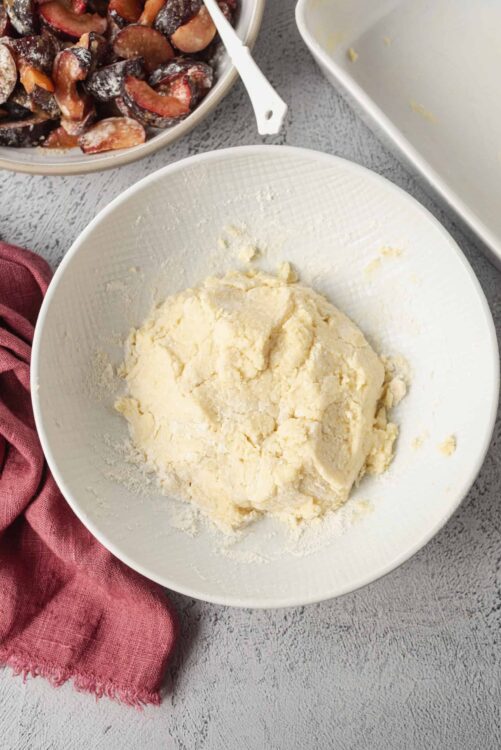 Buttery pie crust dough in a white bowl on a grey surface, with a red cloth nearby.