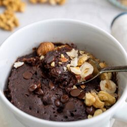Rich chocolate dessert in a white mug with nuts and chocolate chips.