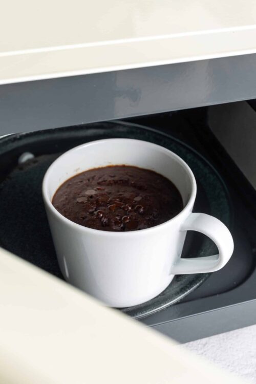 Rich chocolate lava cake in a white mug on a to-go tray, perfect for dessert or coffee break.