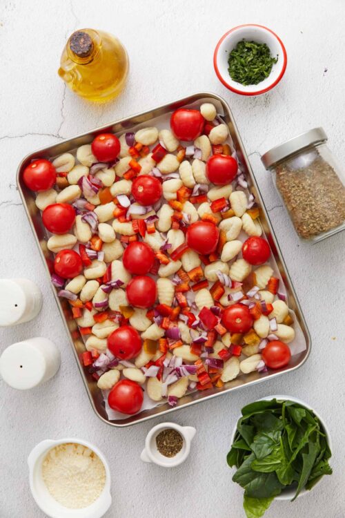 Baked gnocchi with cherry tomatoes, red onions, and colorful vegetables on a baking sheet.