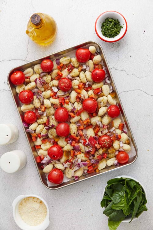 Baked gnocchi with cherry tomatoes, red onion, and herbs ready for roasting.