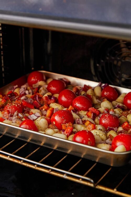 Oven roasted cherry tomatoes, red onions, and potatoes baking in a metal tray.