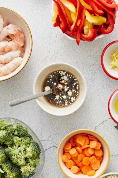 Fresh raw shrimp and assorted colorful sliced vegetables and sauces for cooking or salad preparation.