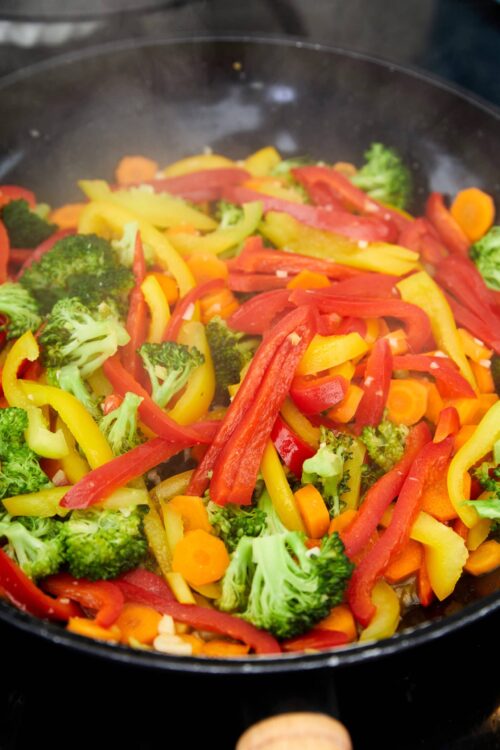 Colorful stir-fried mixed vegetables in a black skillet, including broccoli, bell peppers, and carrots.
