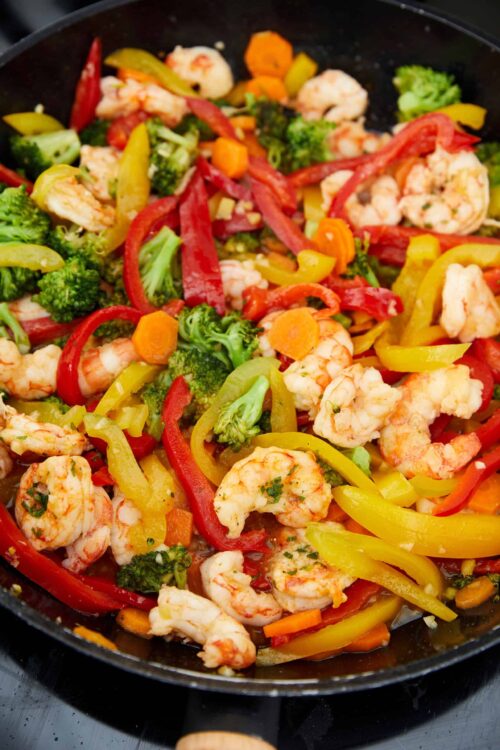 Sautéed vegetables with shrimp, colorful bell peppers, broccoli, and carrots in a skillet.
