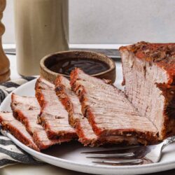 Juicy roasted pork shoulder with crispy crust on plate with dipping sauce.