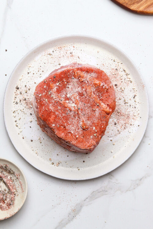 Juicy seasoned beef heart on a white plate with spices.