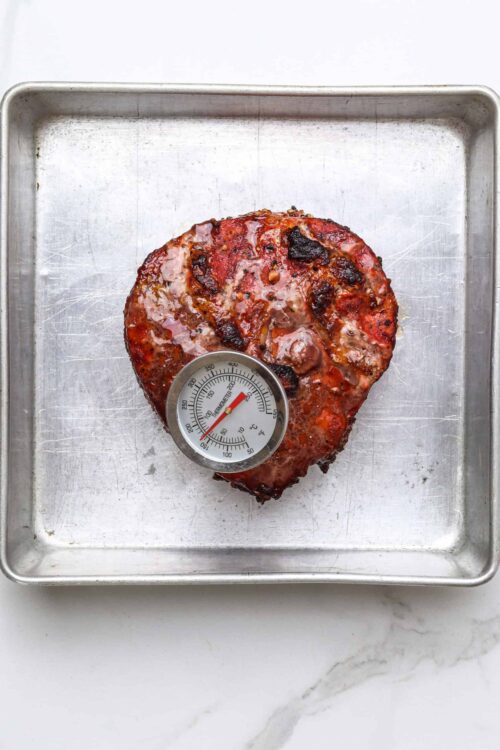 Juicy baked ham with a thermometer on a baking sheet.