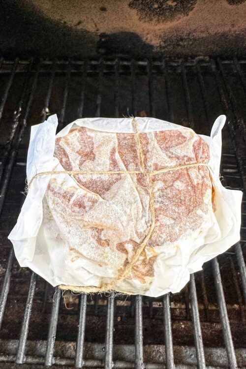 Juicy marinated steak wrapped in parchment paper on oven grill rack.