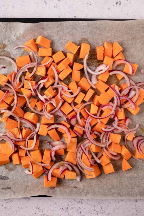 Sweet potato cubes and sliced red onions on baking sheet for roasted vegetables.