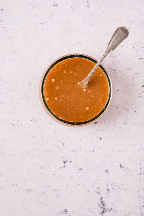 Creamy peanut sauce in a glass jar with a silver spoon, perfect for dipping and dressing.