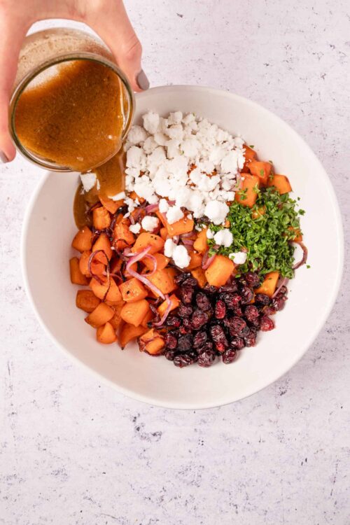 Sweet potato salad with cranberries, feta, herbs, and balsamic dressing on white bowl.