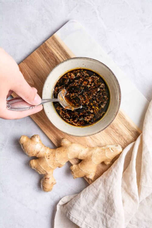 Savory garlic-ginger soy sauce in a bowl, fresh ginger root on a wooden cutting board, light background.