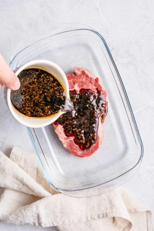 Marinade being poured over raw steak in glass baking dish, highlighting beef marinade for tender meat.