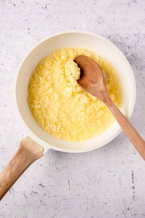 Mashed potatoes in a white bowl with a wooden spoon, ready to serve.