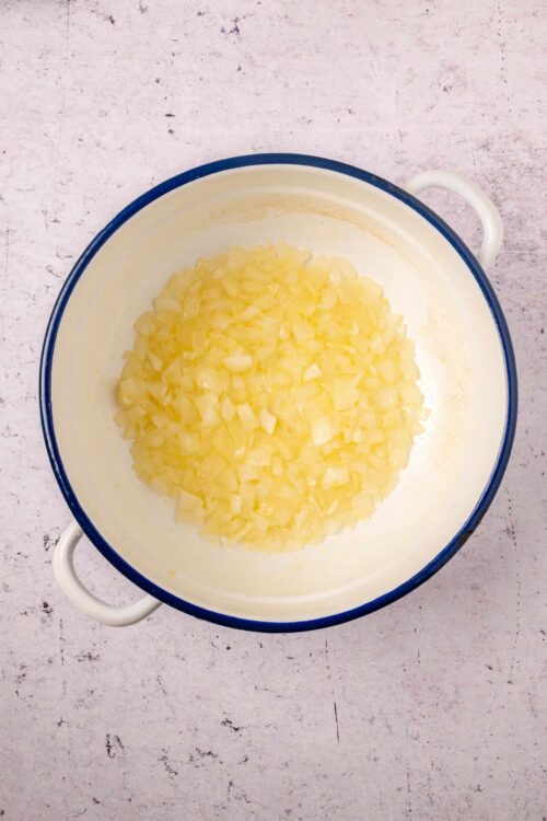 Diced onions in a white enamel mixing bowl with blue rim on a textured surface.