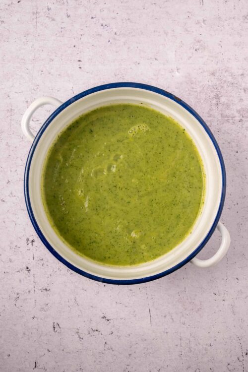 Creamy green vegetable soup in a white and blue bowl, served with fresh herbs and vegetables. Perfect for healthy, homemade meals.