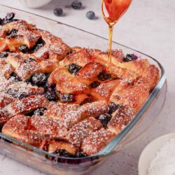 Sweet blueberry cobbler with golden, flaky crust and a drizzle of honey, served in a glass baking dish for dessert.