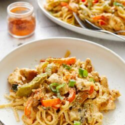 Creamy chicken and vegetable pasta dish topped with green onions on a white plate.