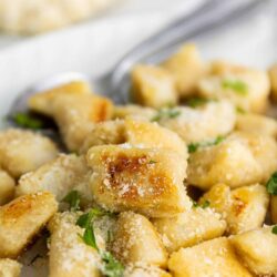Crispy gnocchi with grated Parmesan and fresh herbs on white plate.