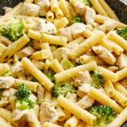 Creamy chicken and broccoli pasta in a black skillet with grated cheese on top.