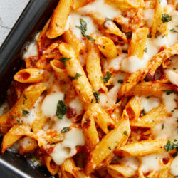 Creamy baked penne pasta with tomato sauce and melted cheese, garnished with fresh herbs.