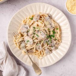Creamy mushroom pasta dish served on a beige plate with fresh herbs and grated cheese.