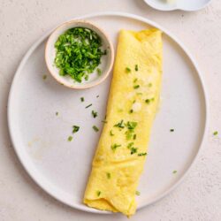 Fluffy scrambled eggs garnished with chopped chives on a white plate.