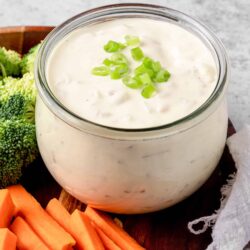 Creamy ranch dip with chopped green onions in a glass jar, served with fresh vegetables for snacking or appetizers.
