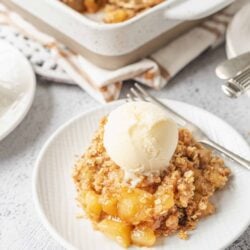 Sweet apple crumble pie with vanilla ice cream on a white plate.