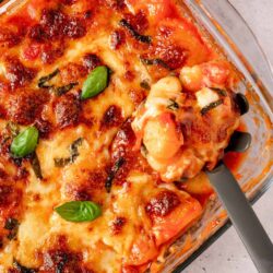 Baked cheesy lasagna with basil and tomato sauce in a glass dish.