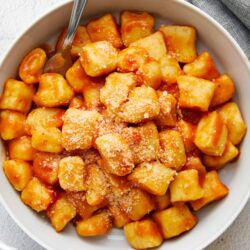 Crispy cheese tortellini with tomato sauce and grated Parmesan cheese in a white bowl.