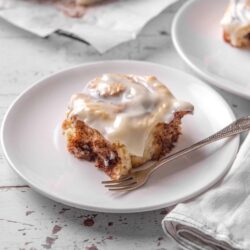 Butter pecan cinnamon roll cake with white glaze, sliced on a white plate.