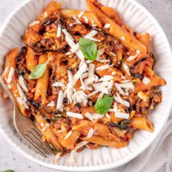 Pasta with tomato sauce, cheese, and basil in a white bowl.
