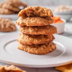 Soft and chewy oatmeal cookies stacked on white plate with a textured gray background.