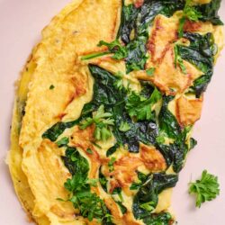 Creamy spinach and cheese omelette with fresh herbs on a white plate.