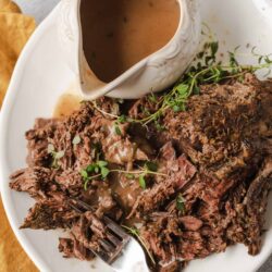 Tender slow-cooked pot roast with gravy and herbs on a white plate.