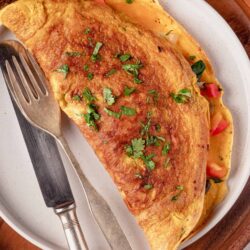 Golden-brown omelette with fresh herbs on white plate.